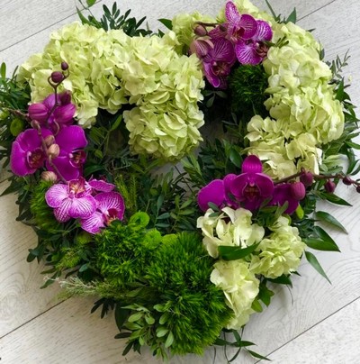 Open heart with green hydrangea, cerise phanelopsis orchid, green carnations, button chrysanthemums and wild foliage. By Croydon Blooms florist
