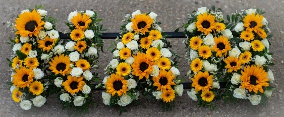 Beautiful bright funeral tribute to include mini sunflowers and yellow daisies with white lysanthius and spray roses. by Croydon Florist