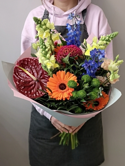 florist holding vibrant bouquet to include Anthurium, green chrysanthemum, orange gerbera, blue delphinium tied in a hand tied in Croydon Flower Shop, for same day delivery in Selhurst, Waddon, Mitcham, East Croydon, South Croydon, Purley, Coulsdon, Kenley, Wallington, Beddington, Woodcote, Selsdon, Chipstead,