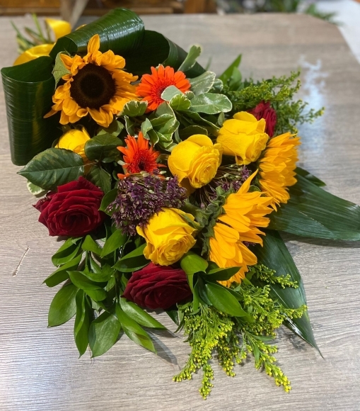 This summer vibe sheaf is a mix with Sunflowers, orange daisies, Red Roses and seasonal alium, solidago. By Croydon Blooms florist