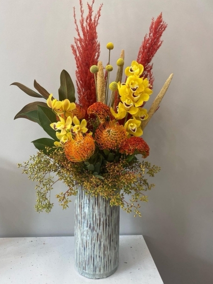 Tropical flowers vase with Protea, Cymbidium orchid, dry Pampas grasses in tall green vase by florist in Croydon