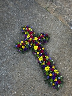 Mixed flowers vibrant cross with cerise roses, yellow daisy, yellow spray roses, purple Lisanthius, lilac fillers. Made by florist in Croydon, Surrey, UK